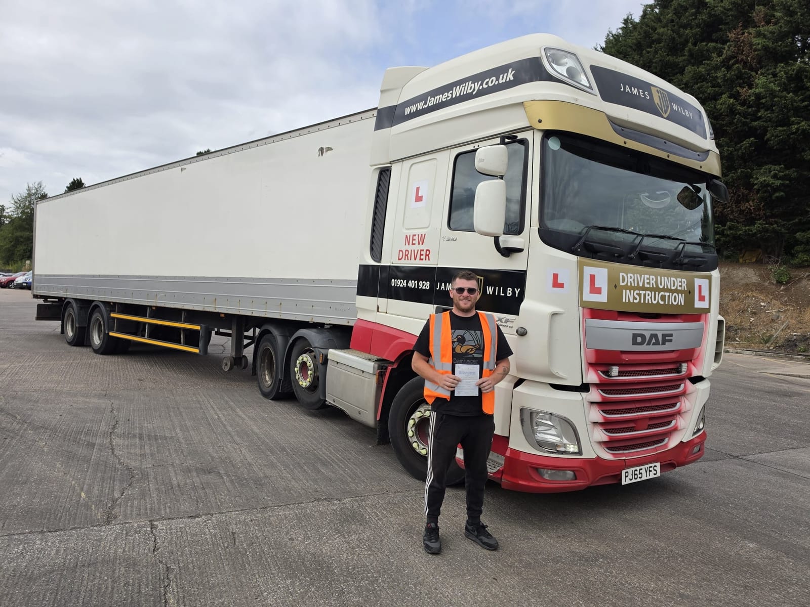 Conor Redgwick holding a Class 1 pass certificate beside a James Wilby training HGV
